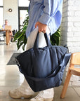 Person holding large puffy navy nylon tote bag with crossbody strap
