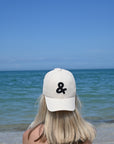 Person wearing a white cap with a black ampersand symbol at the beach
