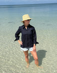 Person wearing a black shirt and straw hat standing in clear water with a blue sky background