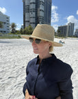 Person on the beach wearing a straw fedora hat with building in the background