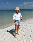 Person wearing a straw bucket hat standing on a sandy beach with ocean and blue sky in the background