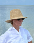 Person wearing a straw hat and sunglasses with a body of water in the background