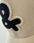 Beige cap with a black ampersand symbol on a white background