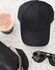 Black cap with 'Living Goodness' text, sunglasses, and a drink on a textured surface