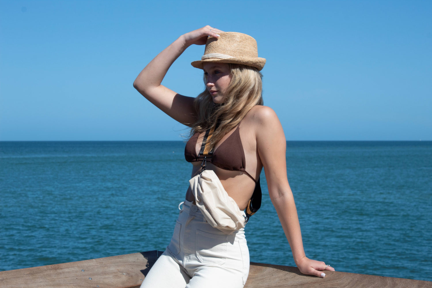Person at the pier wearing the Orlando sand crossbody belt bag and straw essential hat