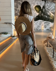 person wearing the tower hat and holding the gabie medium sized hyancinth straw bag with black leather handles and black crossbody strap