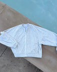 A light heather gray zip-up jacket with a stand collar and elastic cuffs, laid flat on a concrete poolside surface.