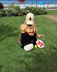 Person sitting on grass with a paddle and ball, wearing a cap with a black ampersand logo.