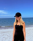 Person at the beach wearing a black outfit and black baseball cap