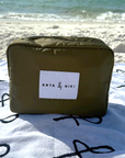 Green pouch with 'Anya & Niki' label on a beach towel