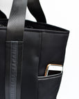 Close up of exterior pocket on black neoprene tote bag with high shine cinch top closure and leather details.