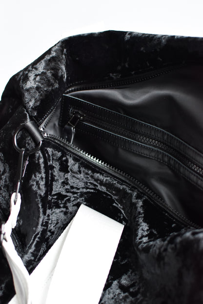Close up of interior lining on black velour duffel bag with white straps and leather details. 