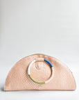 Pink half-moon straw clutch with colorful wrapped circle handle and leather sides.