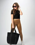 Person holding the Anya & Niki Hawthorne Tote - a black neoprene tote bag with high shine cinch top closure and leather details.