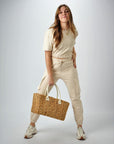 Person holding the Anya & Niki Augustine straw bag - a midsized hyacinth straw tote with cream leather handles and linen cinch top.