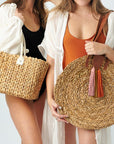 Two people holding Anya & Niki straw bags, the Augustine hyacinth midsized straw tote with leather handles and the Palmdale circle straw tote with suede tassel detail and leather handles.