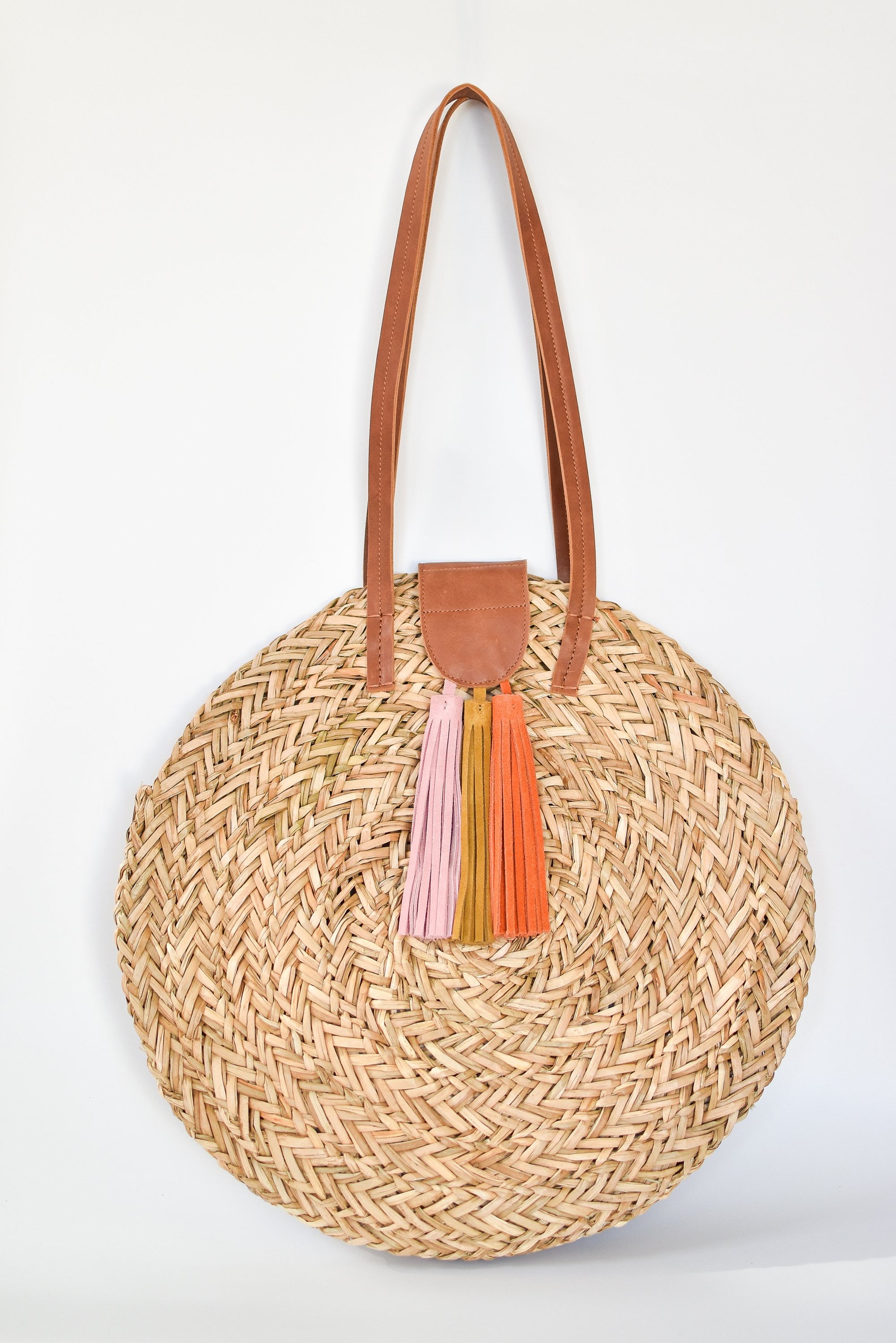 Natural seagrass round straw bag with leather handles and suede tassel closure.