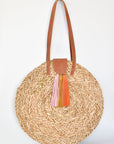 Natural seagrass round straw bag with leather handles and suede tassel closure.