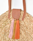 Close up of natural seagrass round straw bag with leather handles and suede tassel closure.
