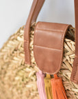 Close up of natural seagrass round straw bag with leather handles and suede tassel closure.