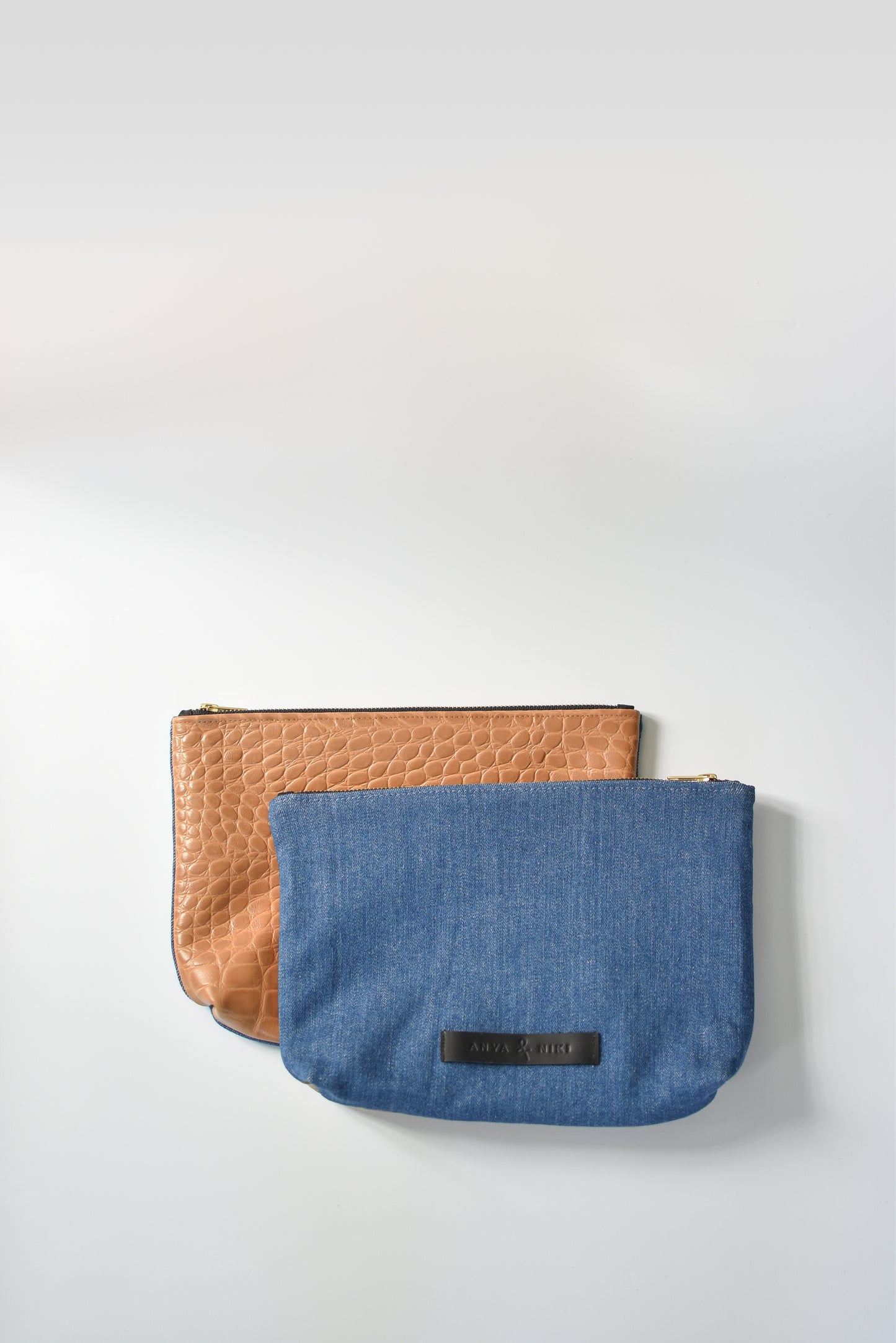 Medium wash denim and caramel colored embossed leather skin medium pouch with brass zipper and leather logo label.