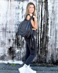 Person holding the Anya & Niki Davie Backpack. A black nylon convertible backpack tote with leather details.