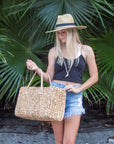 Person holding the Fullerton Straw Tote - a large natural hyacinth straw tote with matching leather handles.