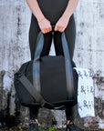 person holding black mesh duffel bag with leather trim details and black glossy liner.