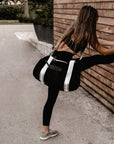 person wearing black velour duffel bag with white straps and leather details, while stretching on wood wall.