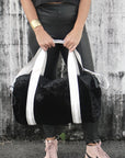 person holding black velour duffel bag with white straps and leather details