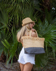 person holding natural raffia straw tote with linen lining and gray color block base.