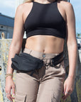 Person wearing black nylon belt bag with black crossbody strap with shiny black leather detail
