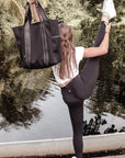 Person holding the Anya & Niki Hawthorne Tote - a black neoprene tote bag with high shine cinch top closure and leather details.