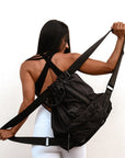 Person holding the Anya & Niki Davie Backpack. A black nylon convertible backpack tote with leather details.