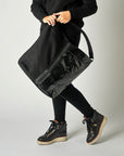 person with black mesh and glossy vinyl sporty tote bag with black leather and webbing details.