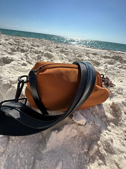Brown nylon belt bag with black crossbody strap and shiny black leather detail on the beach