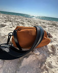 Brown nylon belt bag with black crossbody strap and shiny black leather detail on the beach