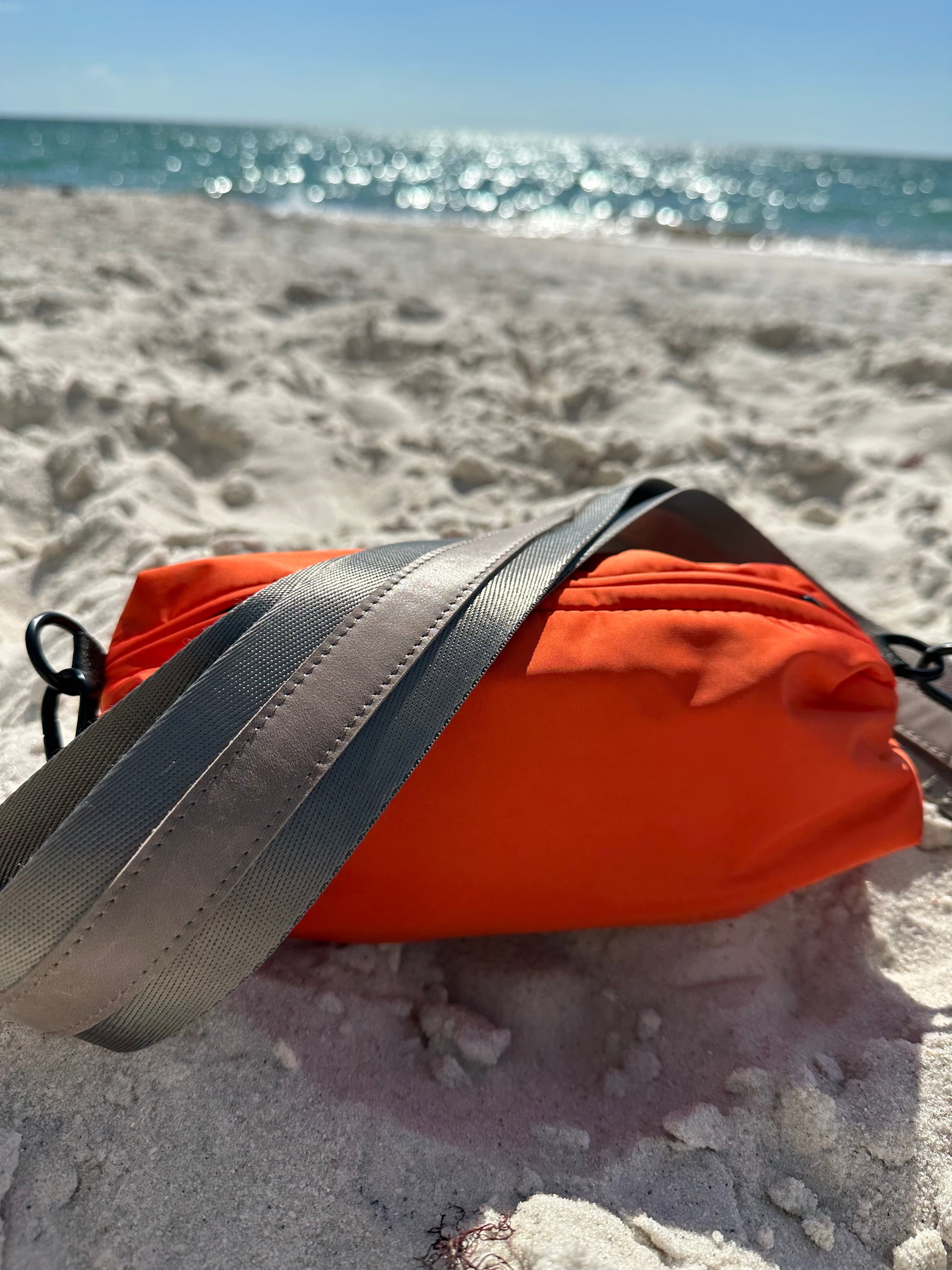 Orange nylon belt bag with grey crossbody strap and grey leather detail at the beach