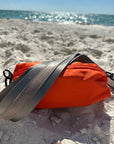 Orange nylon belt bag with grey crossbody strap and grey leather detail at the beach