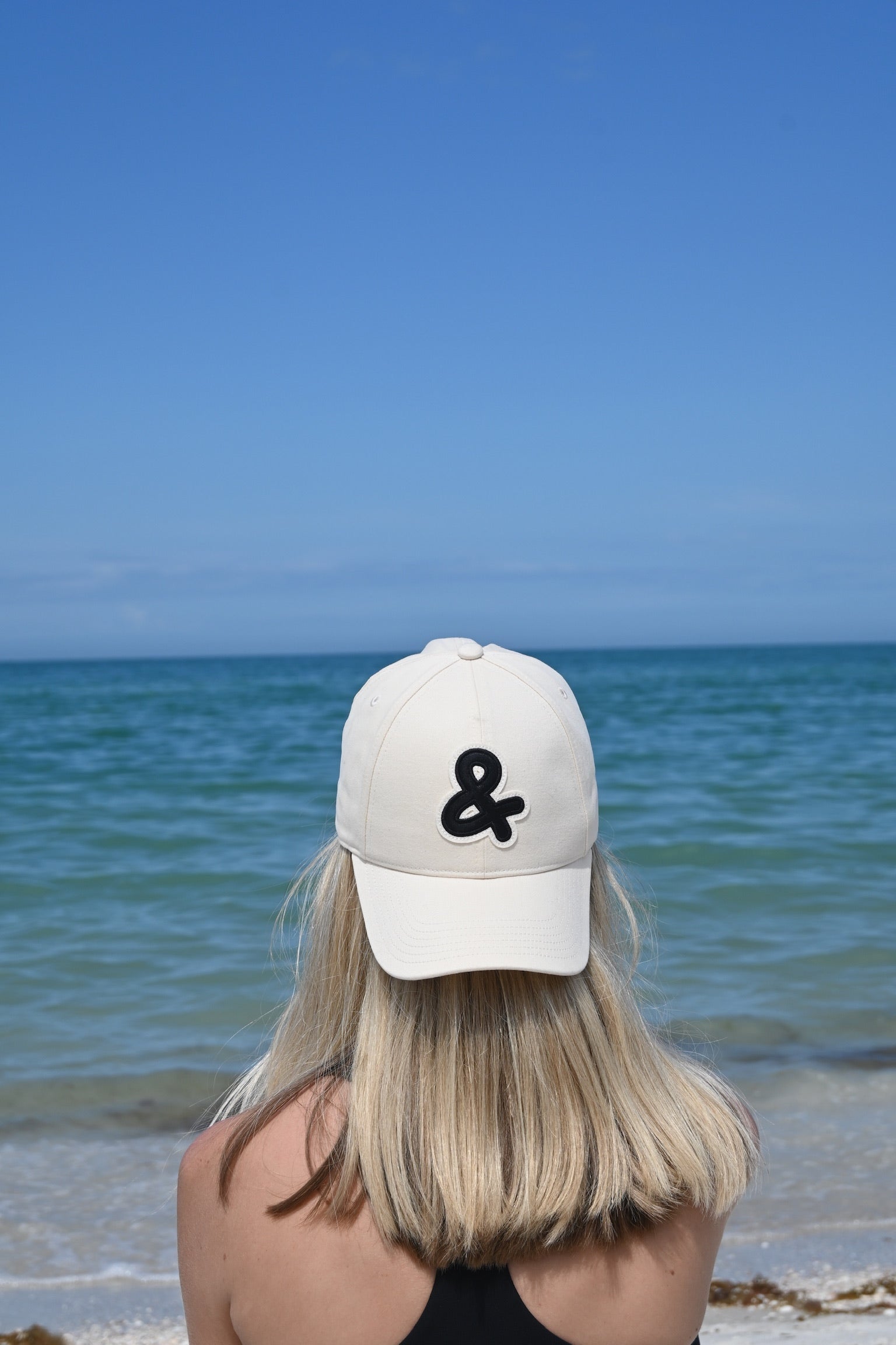 Person wearing a white cap with a black ampersand symbol at the beach