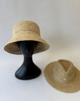 Two straw hats on a white background, one on a black mannequin head and the other on a flat surface.
