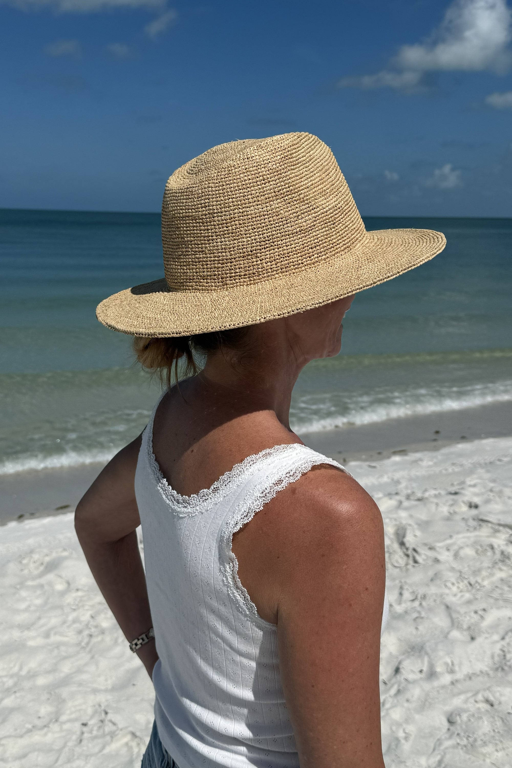 Person wearing a straw hat and white sleeveless top on a beach