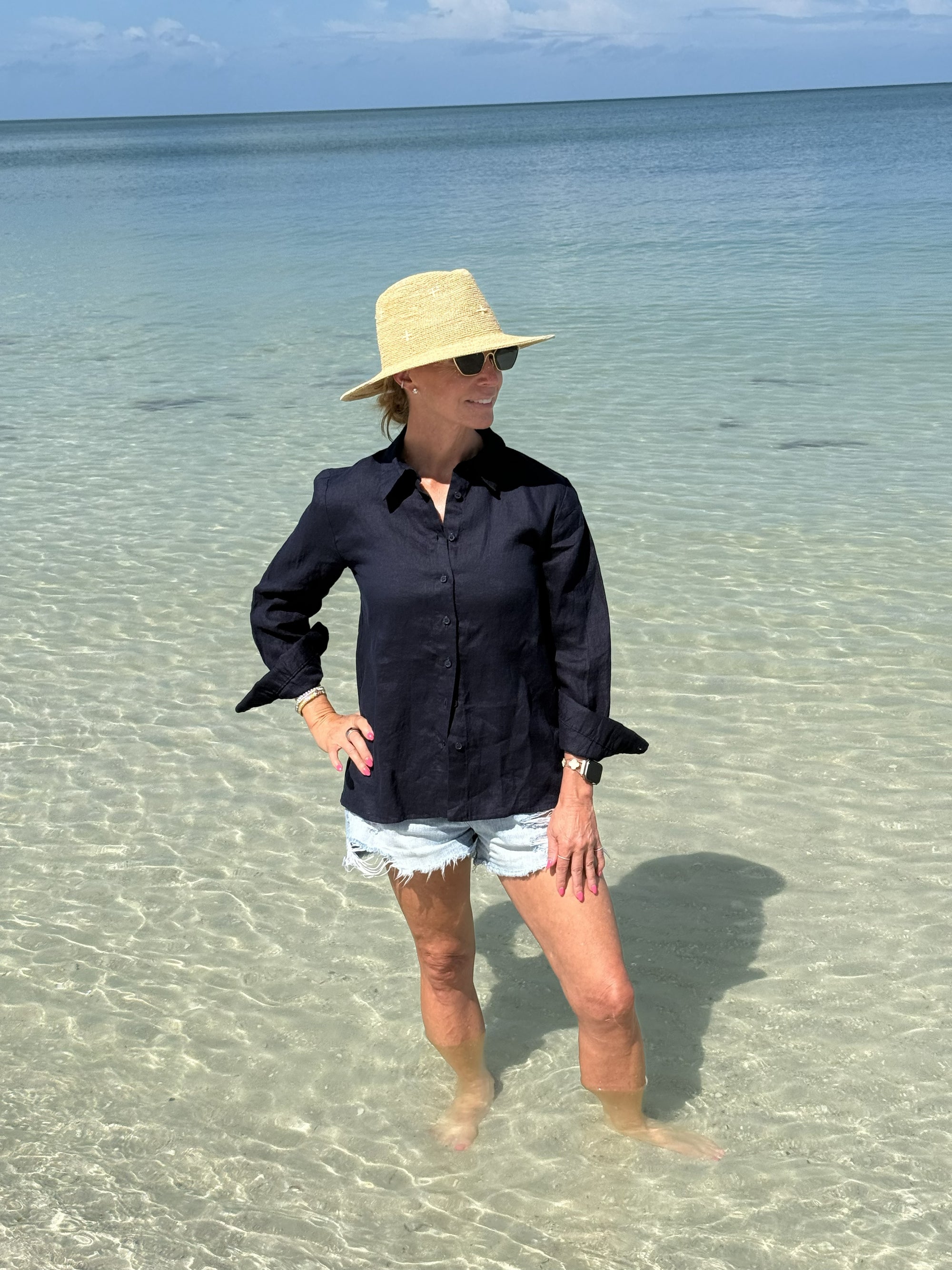 Person wearing a black shirt and straw hat standing in clear water with a blue sky background