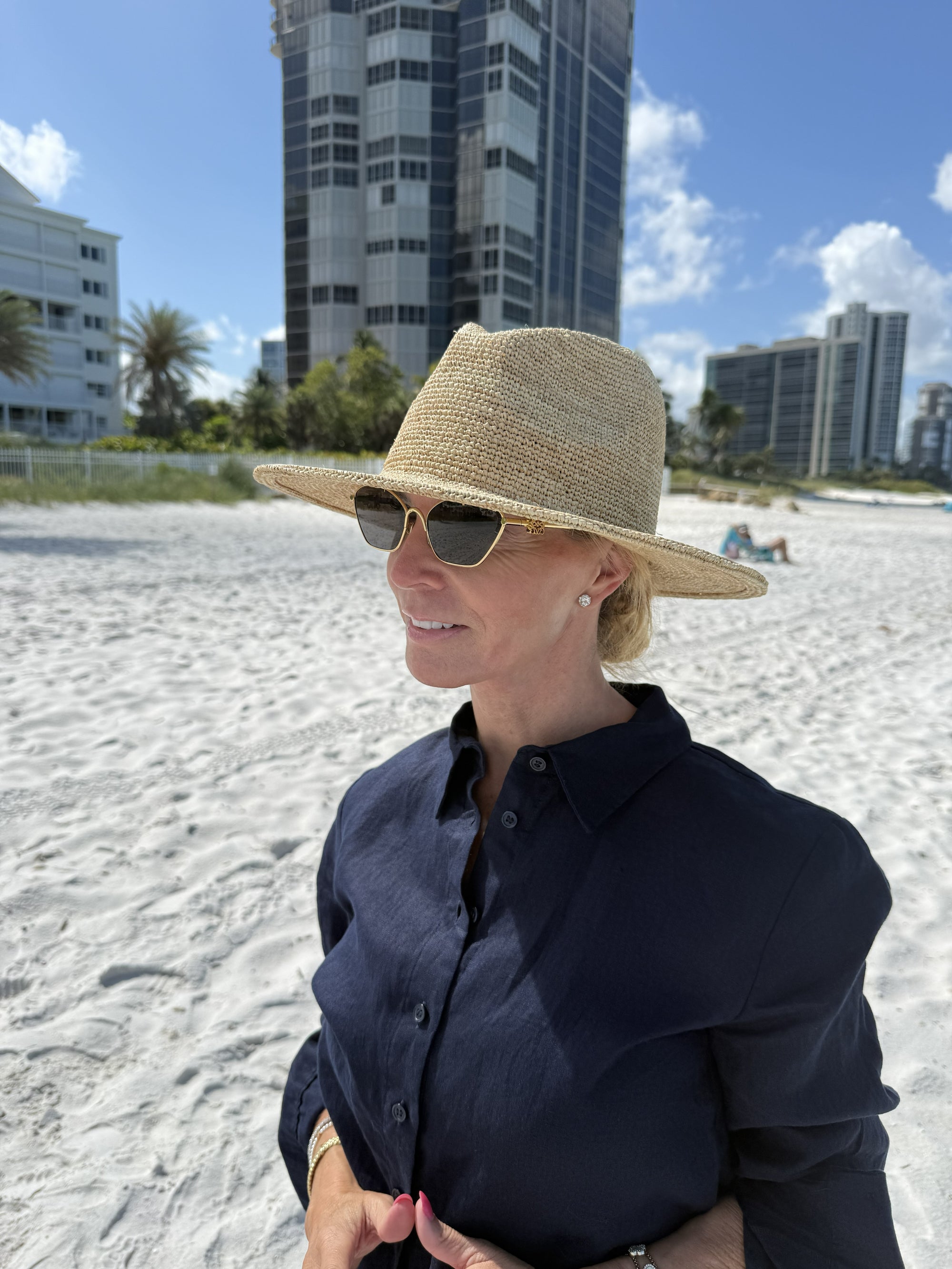 Person on the beach wearing a straw fedora hat with building in the background