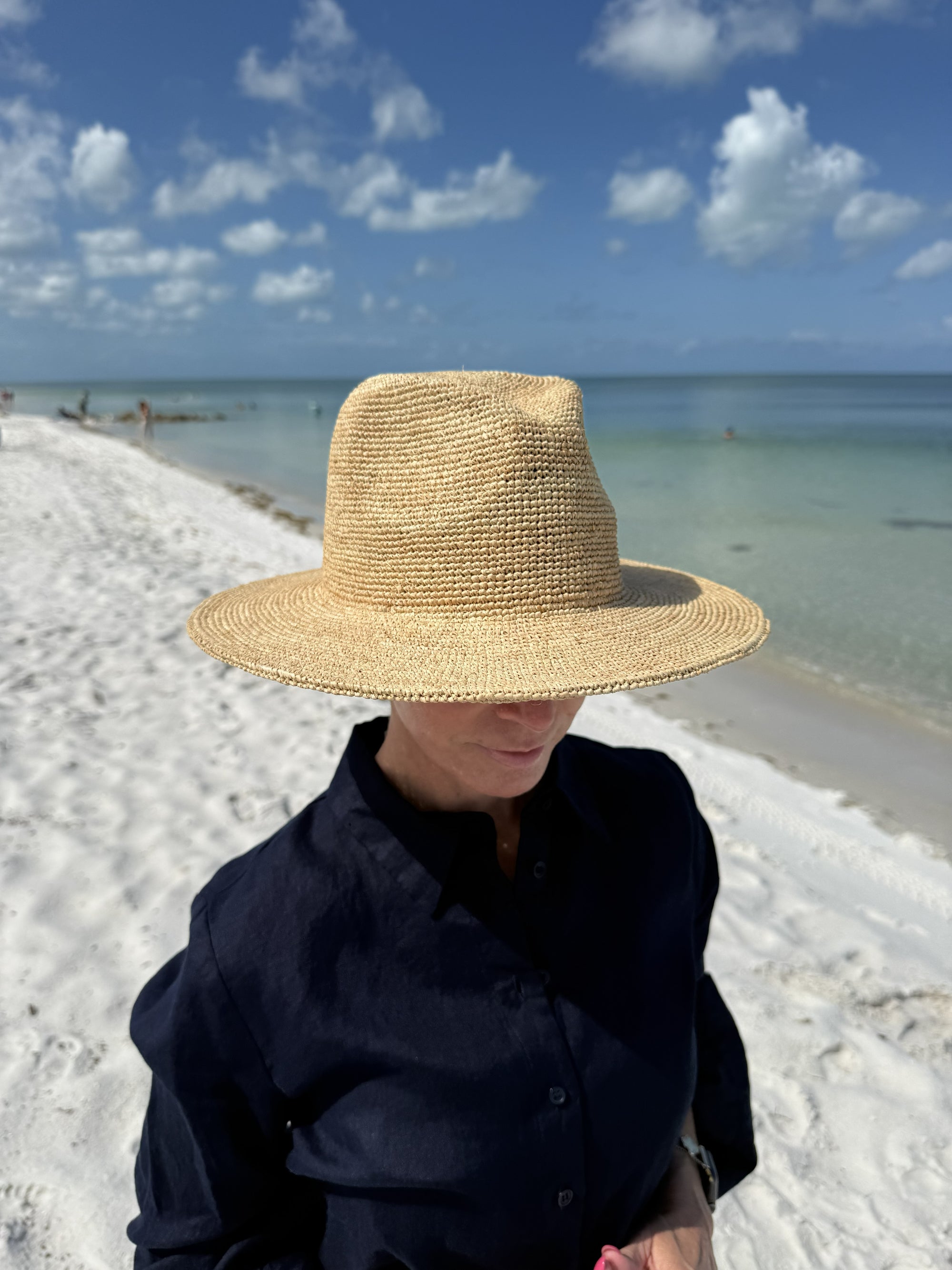 Person on the beach wearing a straw fedora hat and a black shirt
