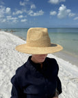 Person on the beach wearing a straw fedora hat and a black shirt