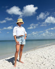 Person wearing a straw bucket hat standing on a sandy beach with ocean and blue sky in the background