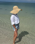 Person wearing a wide-brimmed hat standing in shallow water on a beach.