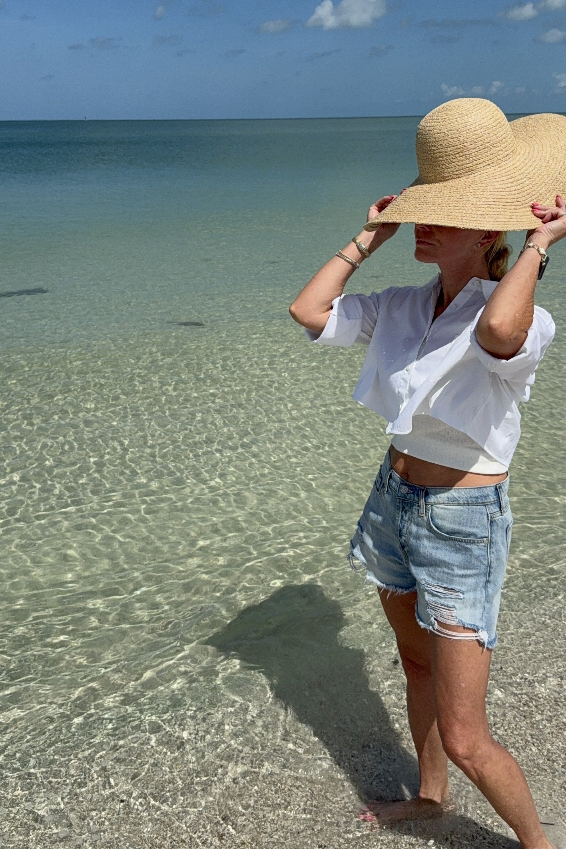 Person wearing a wide-brimmed hat standing in shallow water on a beach.