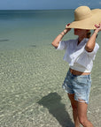 Person wearing a wide-brimmed hat standing in shallow water on a beach.